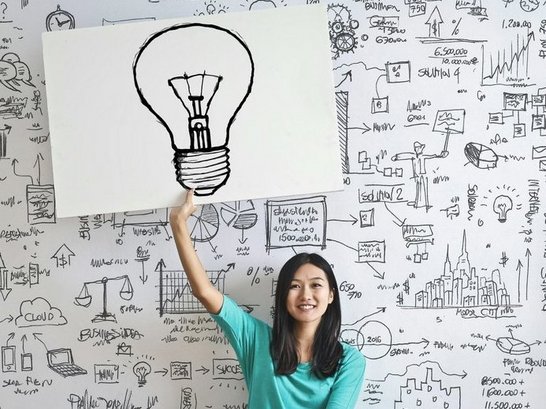 Frau sitzt am Boden und hät ein Schild mit einer aufgezeichneten Glühbirne in der linken, hochgestreckten Hand.