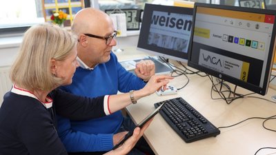 Eine Frau und ein Mann sitzen gemeinsam vor zwei Computerbildschirmen.