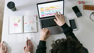 Die Hände von zwei Personen vor einem aufgeklappten Laptop und Kalender.