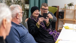 Aufnahme eines digital Überall Workshops. Drei Personen sind zu sehen wobei die einzige Frau am Bild ein Smartphone in der Hand hält.