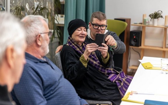 Aufnahme eines digital Überall Workshops. Drei Personen sind zu sehen wobei die einzige Frau am Bild ein Smartphone in der Hand hält.