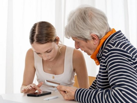 Junge Frau erklärt einer Seniorin etwas auf einem Smartphone.