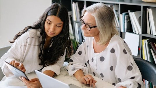 Junges Mädchen erklärt älterer Frau etwas auf einem Tablet.