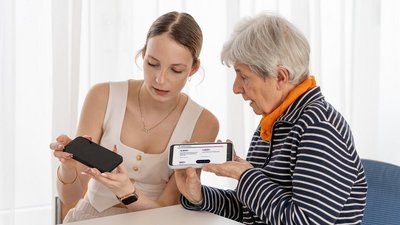 Junge Frau erklärt einer Seniorin etwas auf einem Smartphone.
