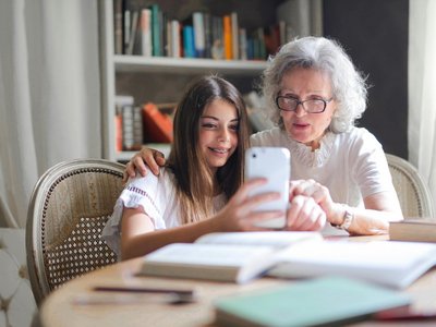 Junges Mädchen erklärt älterer Dame etwas auf einem Smartphone.