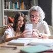 Junges Mädchen erklärt älterer Dame etwas auf einem Smartphone.