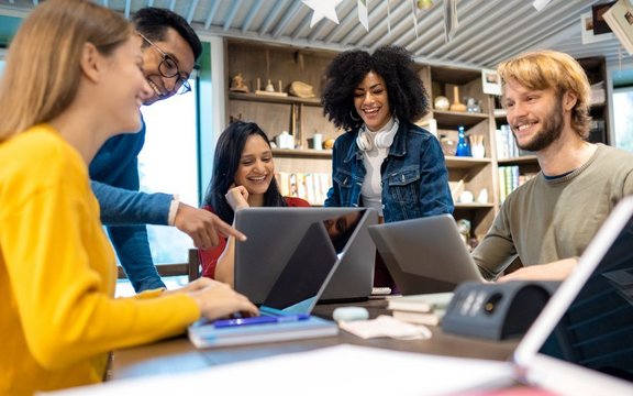 Fünf Menschen rund um einen Tisch, jeder mit Laptop vor sich.
