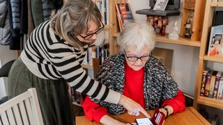 Eine Frau erklärt einer älteren Frau etwas auf dem Smartphone.