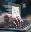 Zwei Hände tippen auf der Tastatur eines Laptops. Über ihnen ist ein weißes E-Mail Icon eingefügt.