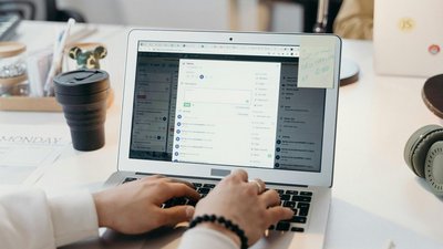 Zwei Hände auf der Tastatur eines aufgeklappten Laptops.