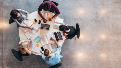 Fünf Personen an einem runden Tisch sitzend von oben fotografiert.