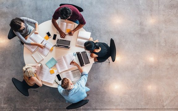 Fünf Personen an einem runden Tisch sitzend von oben fotografiert.