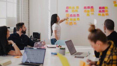 Frau steht vor einem Whiteboard und unterrichtet eine Gruppe von Personen.